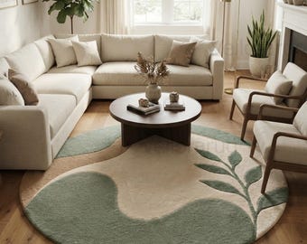 May include: A large round area rug featuring a cream-colored base with sage green organic shapes and a prominent leafy branch design. The rug has a textured pile and is positioned on a light brown wooden floor in a living room setting.