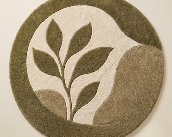 May include: A circular tufted rug featuring a deep olive green border and a central cream-colored field. The design includes a stylized olive green leafy branch motif and an abstract olive green shape on the right side of the rug.