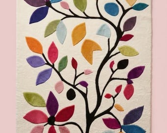 May include: A rectangular area rug with an off-white background featuring a black tree silhouette. The branches are adorned with numerous leaves in various colors including purple, blue, green, yellow, orange, pink, and light blue.
