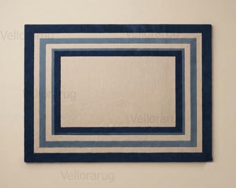 May include: A rectangular area rug featuring a series of concentric borders in alternating shades of dark navy blue, light blue, and beige. The center of the rug is a solid beige rectangle, surrounded by nested frames of blue and beige tones.