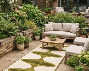 May include: A rectangular area rug featuring a cream-colored background with a bold, olive green abstract wave pattern running through the center. The rug is placed on a stone patio surface, showcasing a distinct, continuous, and flowing design.