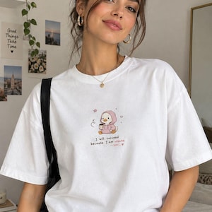 May include: A white short-sleeved t-shirt featuring a small graphic of a cartoon duck wearing a pink hoodie and holding a coffee cup. Below the duck, the text reads, "I will succeed because I am insane," accompanied by small heart and star icons.