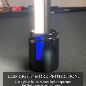 May include: A black glass jar with a bright white light source inserted into the opening. The text on the image reads: LESS LIGHT. MORE PROTECTION. Dark glass helps reduce light exposure for light-sensitive dry goods. Light demonstration only.