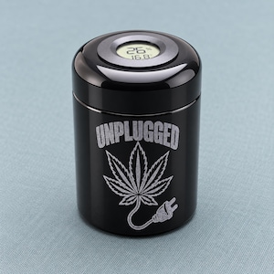 May include: A cylindrical black storage canister with a digital hygrometer display on the lid. The front features an engraved design of a cannabis leaf with an electrical plug tail and the text UNPLUGGED in a bold, sans-serif font.