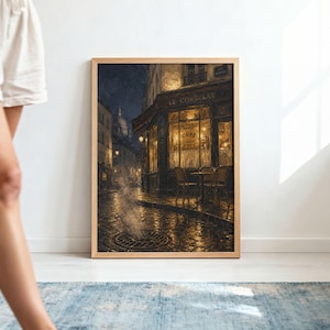May include: A framed wall art print depicting a nighttime street scene of a Parisian cafe named Le Consulat. The image features a cobblestone street with steam rising from a drain, warm golden light emanating from the cafe windows, and chairs.