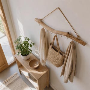 Peut inclure: Un porte-manteau mural composé d'une branche de bois brun clair naturel, suspendu par une corde de jute épaisse. Le support comporte plusieurs crochets métalliques retenant une écharpe en tissu beige, un sac en paille et une veste beige.
