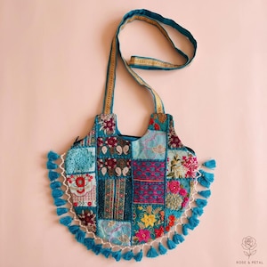 Peut inclure: Un sac à bandoulière bleu sarcelle avec un motif patchwork composé de diverses broderies florales et géométriques dans des tons de rose, jaune et bleu. Le sac possède une longue bandoulière et une frange de petits pompons bleu sarcelle.