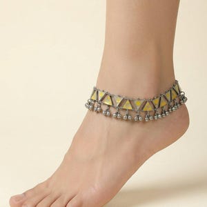 May include: An anklet featuring a series of connected triangular metal links with yellow enamel inlay. The piece is finished with small, round, dangling silver-toned metal charms attached along the bottom edge of the triangular chain structure.
