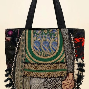 Könnte beinhalten: Eine Tragetasche mit einem Patchwork-Design aus verschiedenen Stoffen in Schwarz, Grün, Rot und Weiß. Die Tasche zeigt gestickte Pfauenmotive, komplexe Muster und einen schwarzen Fransenbesatz an der Unterseite und den Seiten mit zwei schwarzen Henkeln.