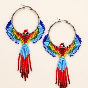 May include: A pair of hoop earrings featuring a beaded parrot design. The parrots are crafted with vibrant red, yellow, green, and blue beads, with long, dangling red beaded tail feathers extending from the bottom of the circular silver-tone hoops.