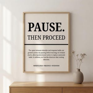May include: A framed wall art print featuring the black text PAUSE. THEN PROCEED in a bold serif font. Below a horizontal line, smaller text reads: The space between stimulus and response holds our greatest power. MINDFULNESS • PRESENCE • INTENTION.