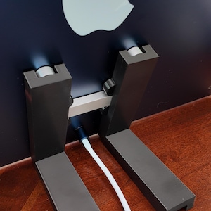 Könnte beinhalten: Ein schwarzer Computerständer mit zwei vertikalen Stützen und einer horizontalen Stange, die diese verbindet. Der Ständer ist so konzipiert, dass er einen Computermonitor anhebt und Kabel ordentlich hält. Der Ständer ist aus robustem Material gefertigt und hat ein elegantes, modernes Design.