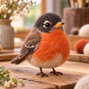 May include: A needle-felted robin figurine featuring a dark brown head, a bright orange chest, and a white belly. The bird has a small yellow beak, black bead eyes, and brown wings with white-tipped feathers, standing on thin brown legs.