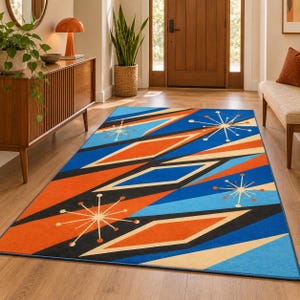 Op de afbeelding: Een rechthoekig vloerkleed met een geometrisch patroon van oranje, blauwe en crèmekleurige ruiten, geaccentueerd door zwarte diagonale strepen en witte sterrenmotieven. Het ontwerp bevat een levendig kleurenpalet over het gehele oppervlak.