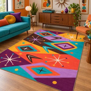 Op de afbeelding: Een rechthoekig vloerkleed met een levendig geometrisch patroon van sterren, boemerangvormen en ruiten in tinten paars, oranje, geel en groenblauw. Het ontwerp bevat een herhalend motief dat is geïnspireerd op het midden van de twintigste eeuw.