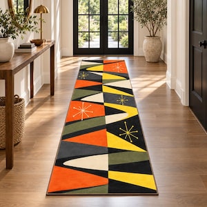 May include: A long rectangular runner rug featuring a geometric pattern of triangles and curved shapes in vibrant orange, yellow, olive green, cream, and black. The design includes thin, starburst-like line motifs scattered across the surface.