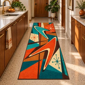 May include: A rectangular runner rug featuring a geometric pattern with large orange and teal boomerang shapes, dark brown accents, and cream-colored starburst motifs on a multi-colored background, laid out on a light-colored speckled floor.