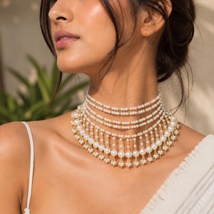 May include: A multi-strand choker necklace featuring rows of small white pearls connected by gold-toned metal links. The design includes a cascading fringe of larger white pearls and small pearl clusters suspended from the lowest strand of the necklace.
