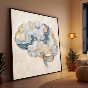 Op de afbeelding: Een groot ingelijst kunstwerk aan de muur met een gestileerde illustratie van een menselijk brein. Het brein is weergegeven in tinten blauw, crème en goud met gedetailleerd lijnwerk, op een getextureerde, lichtbeige achtergrond in een dunne zwarte lijst.
