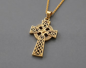 May include: A gold-toned Celtic cross pendant featuring intricate openwork knotwork patterns and a central circular ring, suspended from a matching gold-toned chain. The cross displays detailed interlacing designs within each arm and the center.