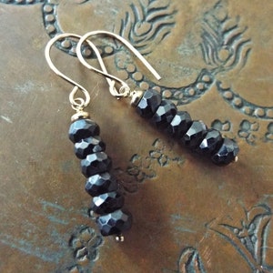 May include: A pair of gold earrings with black faceted beads. The earrings are dangling and have a simple hook closure.