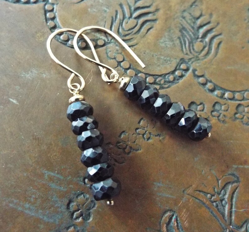 May include: A pair of gold earrings with black faceted beads. The earrings are dangling and have a simple hook closure.