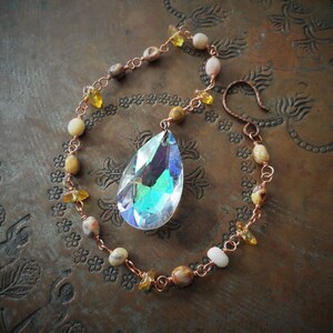 Peut inclure: Un attrape-soleil en fil de cuivre avec un cristal iridescent en forme de larme suspendu. L'attrape-soleil est orné de petites perles brunes, blanches et jaunes.