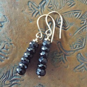 May include: A pair of silver dangle earrings with black faceted beads. The earrings are approximately 2 inches long.