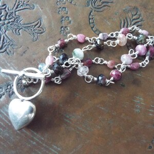 Pode incluir: Um bracelete de corrente de prata com um fecho de cora&ccedil;&atilde;o e pedras preciosas multicoloridas. O bracelete tem um fecho de correr.