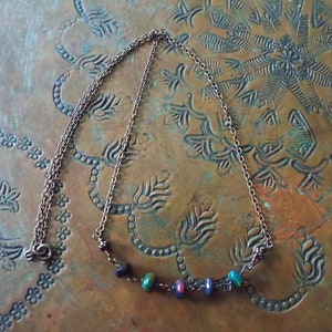 May include: A silver chain necklace with a row of colourful glass beads. The beads are a mix of green, blue, red, and black.