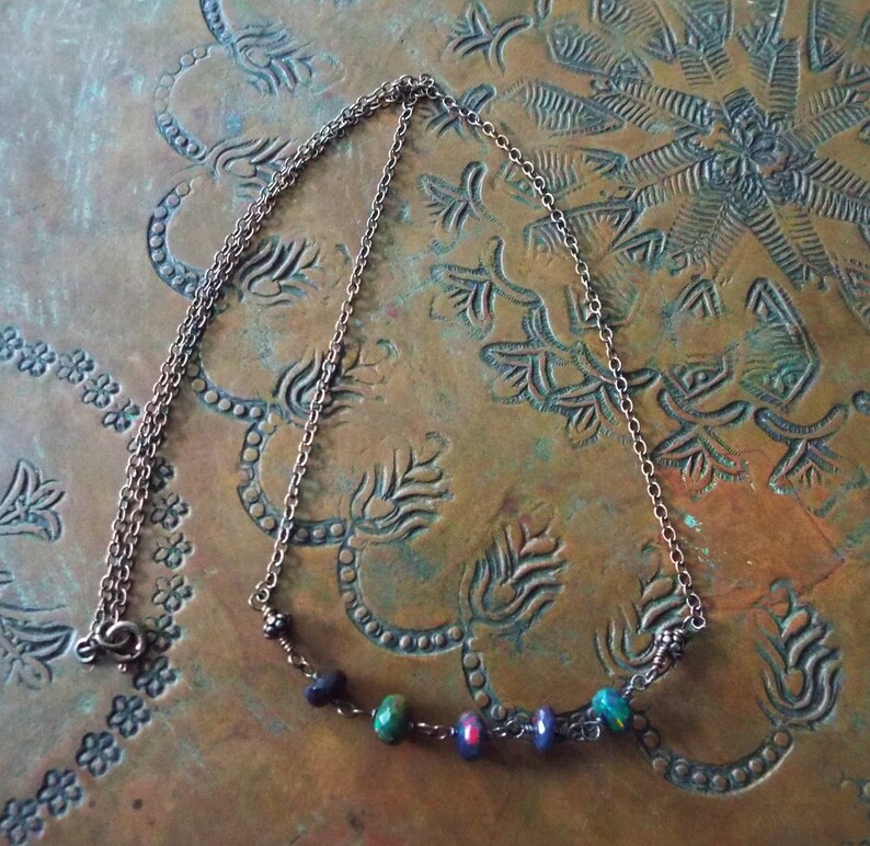 May include: A silver chain necklace with a row of colourful glass beads. The beads are a mix of green, blue, red, and black.