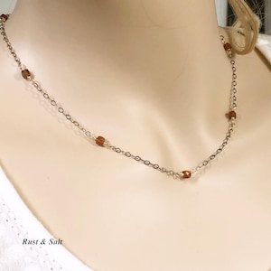 May include: A delicate gold chain necklace with small brown glass beads. The necklace is on a white mannequin.
