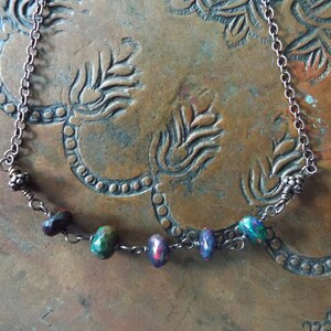 May include: A silver chain necklace with a row of five iridescent gemstone beads. The beads are a mix of purple, green, and blue.