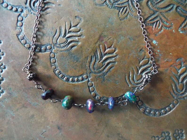 May include: A silver chain necklace with a row of five iridescent gemstone beads. The beads are a mix of purple, green, and blue.