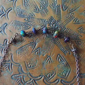 May include: A silver chain necklace with a series of iridescent opal beads and silver accents. The necklace is lying on a textured copper surface.