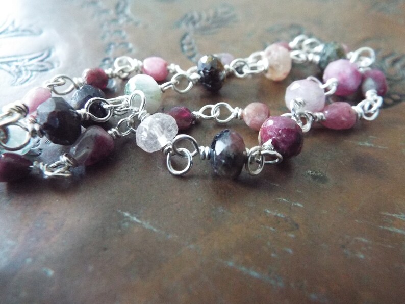 Pode incluir: Um bracelete de corrente de prata com pedras preciosas rosa, verde e preta. O bracelete &eacute; feito com contas envoltas em arame e elos de corrente de prata.