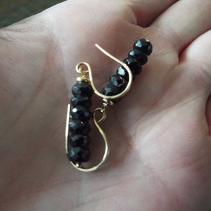 May include: A pair of gold earrings with black beads. The earrings are made with a simple wire design and feature a row of black beads.