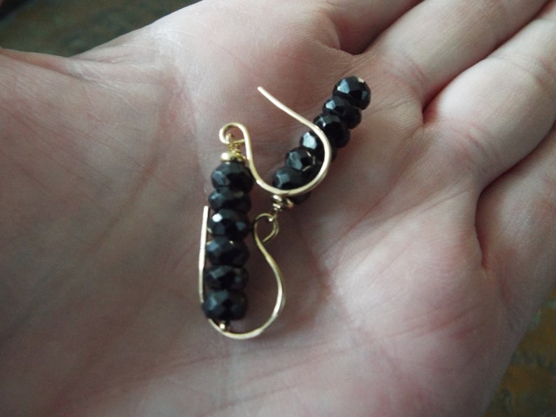 May include: A pair of gold earrings with black beads. The earrings are made with a simple wire design and feature a row of black beads.