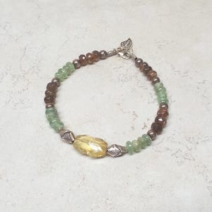 May include: A multi-colored beaded bracelet with a silver leaf charm. The bracelet features green, brown, and yellow beads.