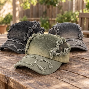 May include: Three five-panel baseball caps featuring a distressed, frayed edge design. The caps are available in black, olive green, and charcoal grey, each with a faded wash finish, metal eyelets on the side panels, and a curved brim.