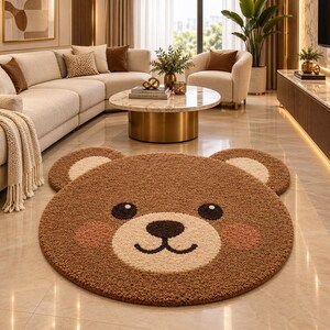 Puede incluir: Una alfombra circular marrón con forma de cara de oso, que presenta un hocico color crema, dos orejas pequeñas redondeadas, ojos marrón oscuro, nariz marrón oscuro, boca curvada y dos parches circulares rosados en las mejillas, de textura.