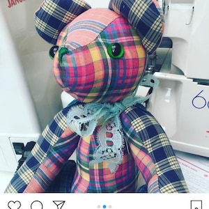 Può includere: Un orsacchiotto di pezza realizzato con toppe di tessuto a quadri multicolore nelle tonalità del rosa, blu, giallo e verde. L'orso presenta occhi a bottone verde brillante, un naso cucito e un nastro di pizzo azzurro legato al collo.