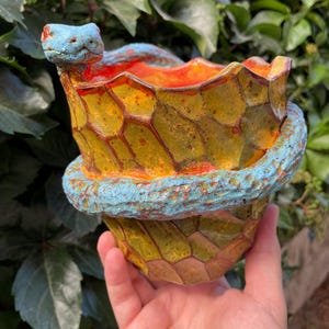 May include: A ceramic planter featuring a textured, yellow and orange honeycomb pattern on the exterior. A sculpted blue snake with a detailed head and body coils around the rim and side of the vessel, creating a decorative and functional container.