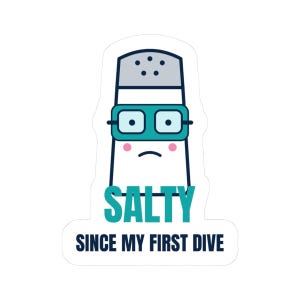 May include: A white salt shaker sticker with a dark blue outline, wearing teal swimming goggles and pink cheeks. The text SALTY is printed in teal, and the text SINCE MY FIRST DIVE is printed in dark blue below the shaker on a white background.