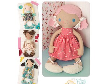 May include: A sewing pattern for making three different dolls. The dolls are all wearing dresses and have pink, brown, and blonde hair. The pattern is from Simplicity and is for "Whimsy Dolls".