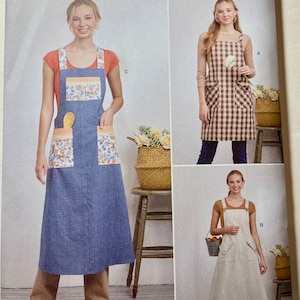 May include: Simplicity sewing pattern featuring three apron designs. One apron is blue with orange floral pockets, another is brown checkered, and the third is white striped. The pattern includes sizes XS-XL and is easy-to-sew.