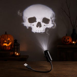 以下が含まれることがあります： 柔軟なネックを備えた黒いUSB給電式プロジェクターライト。壁に明るい白の煙のような頭蓋骨の画像を投影します。このデバイスは、コンパクトな円筒形のヘッドと、調整可能な湾曲したケーブルの端にある標準的なUSBコネクタを備えています。