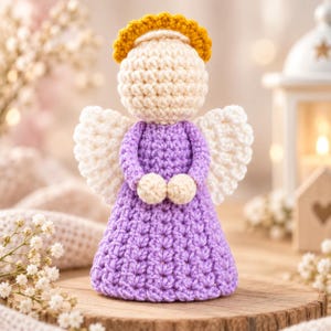 May include: A handcrafted crochet angel figurine featuring a light purple dress, cream-colored head and hands, and white wings. The figure is topped with a textured golden yellow halo, showcasing intricate yarn stitching throughout the entire design.
