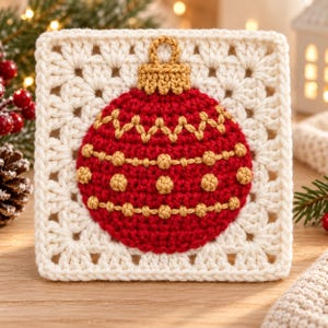 May include: A square crochet granny square featuring a central red Christmas ornament motif. The ornament is detailed with gold yarn embroidery, including a zigzag pattern and rows of small bobbles, topped with a gold crochet cap.