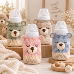 Puede incluir: Cuatro biberones envueltos cada uno en una funda de ganchillo con forma de oso. Las fundas presentan orejas de oso, ojos cerrados y una nariz marrón. Las botellas son de color verde salvia, beige, rosa claro y azul claro, con base crema.